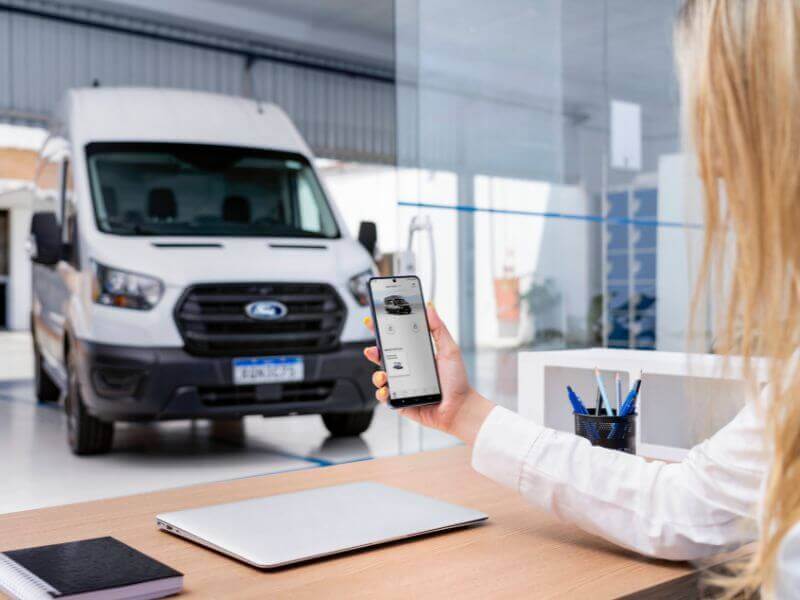 Furgão Ford sendo monitorado via celular por mulher dentro de concessionária