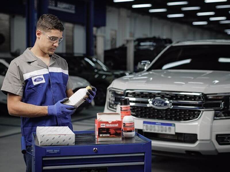 Mecânico Ford escolhendo materiais de manutenção de veículo em frente a uma picape Ford Ranger