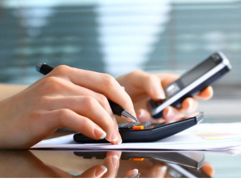 Mãos utilizando calculadora e celular para cálculos