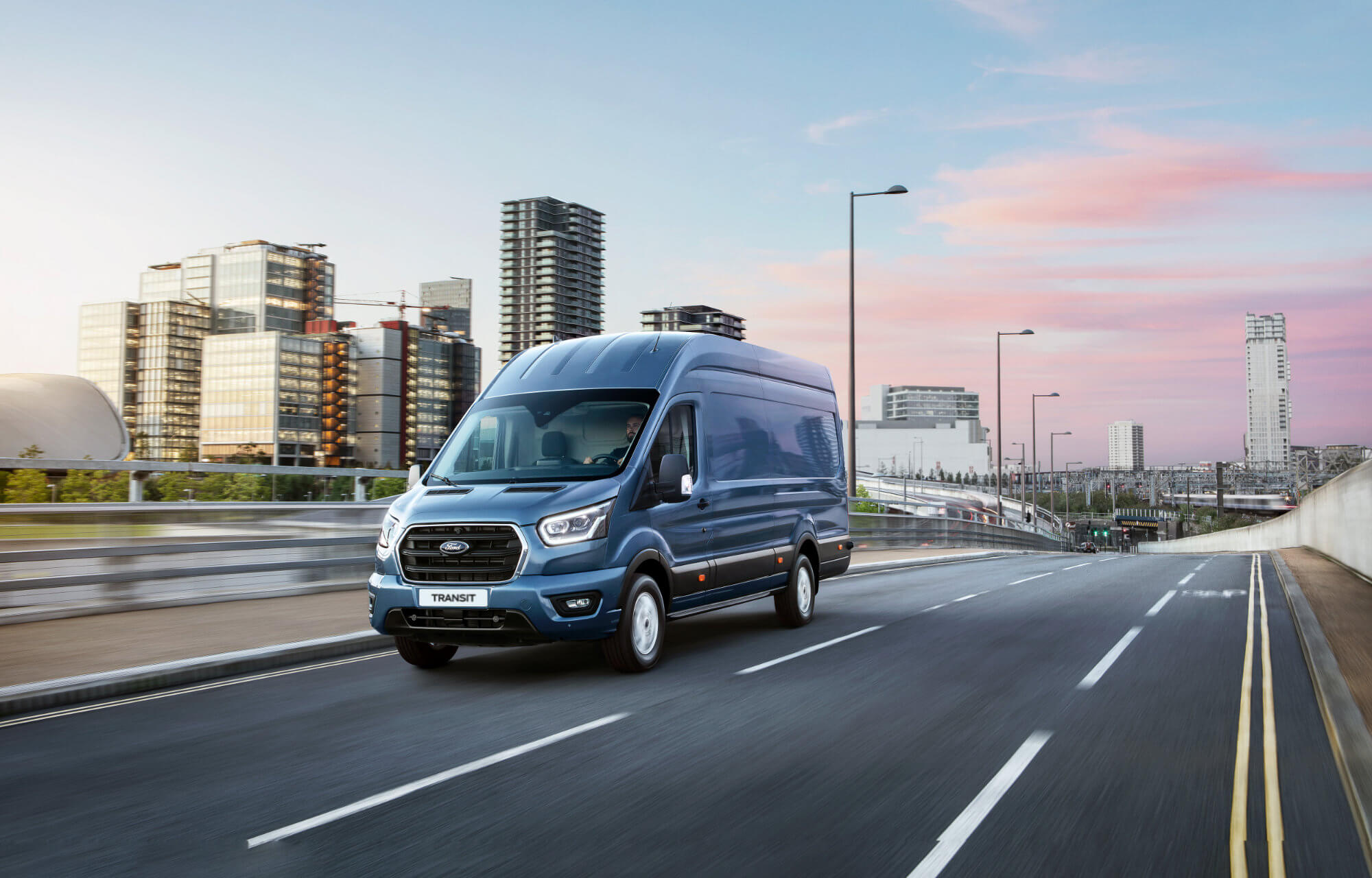 Blauer Ford Transit fährt an Hochhäusern vorbei