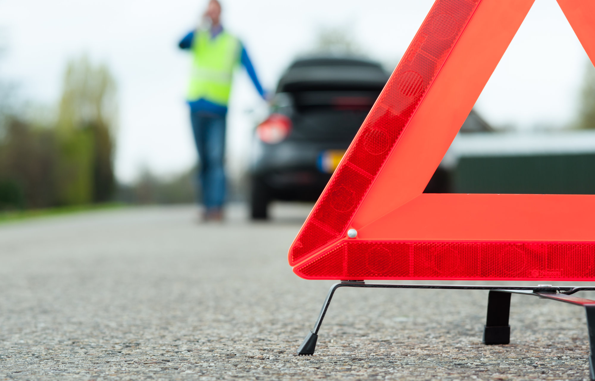 Warndreieck mit Fahrzeug und Mann in Warnweste im Hintergrund